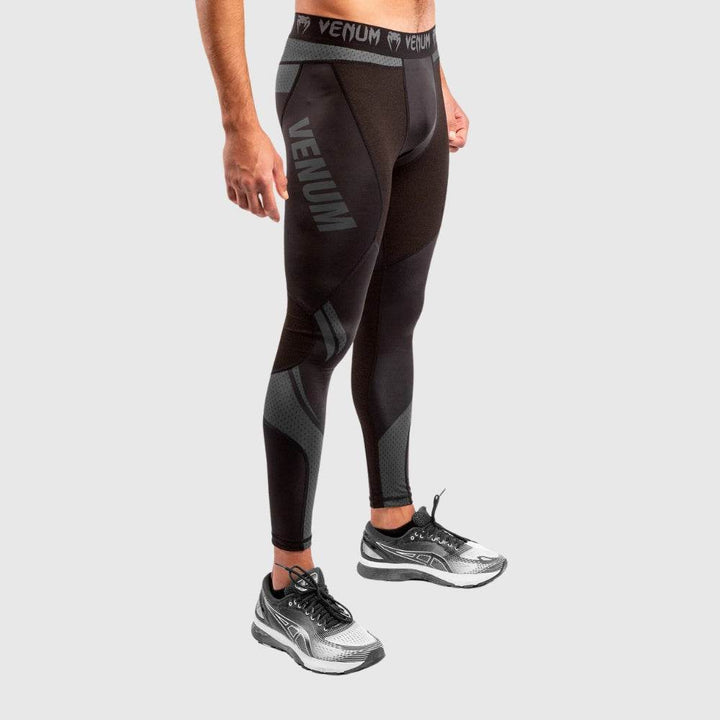 Male model showing left profile in black compression spats with “VENUM” branding in grey on thigh, textured mesh panels visible on calves.