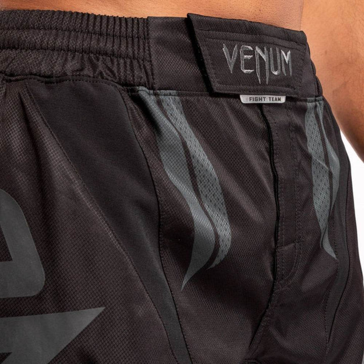 Close-up of the waistband area on Venum shorts showing embroidered "VENUM" patch and subtle dark grey flame-like graphic accents.