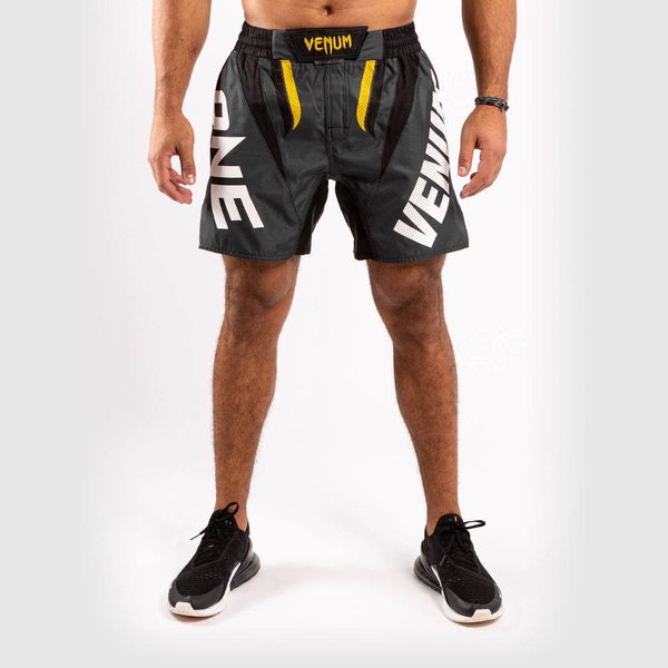 Black Venum fight shorts with “VENUM” and “ONE” text printed in large white letters on each leg. Yellow accents highlight the front waist area.