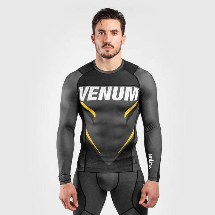 Male model wearing a long-sleeve Venum rash guard in grey with yellow and white VENUM branding across the chest.