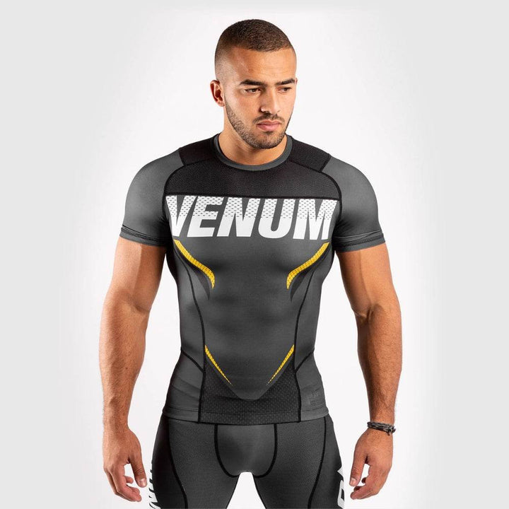 Male athlete in black short sleeve Venum rash guard with bold white "VENUM" print and yellow side accents.
