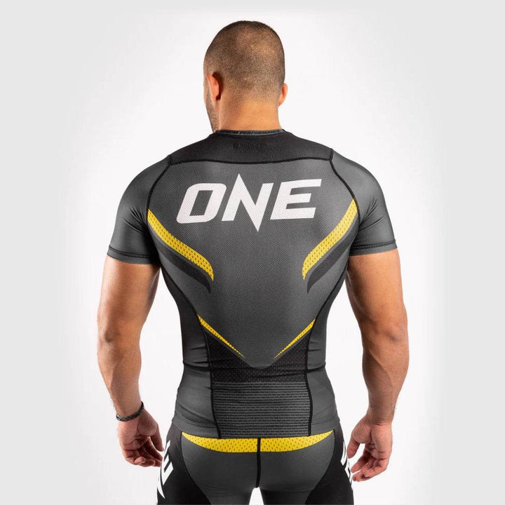 Back of Venum rash guard showing large white "ONE FC" logo and yellow design elements.