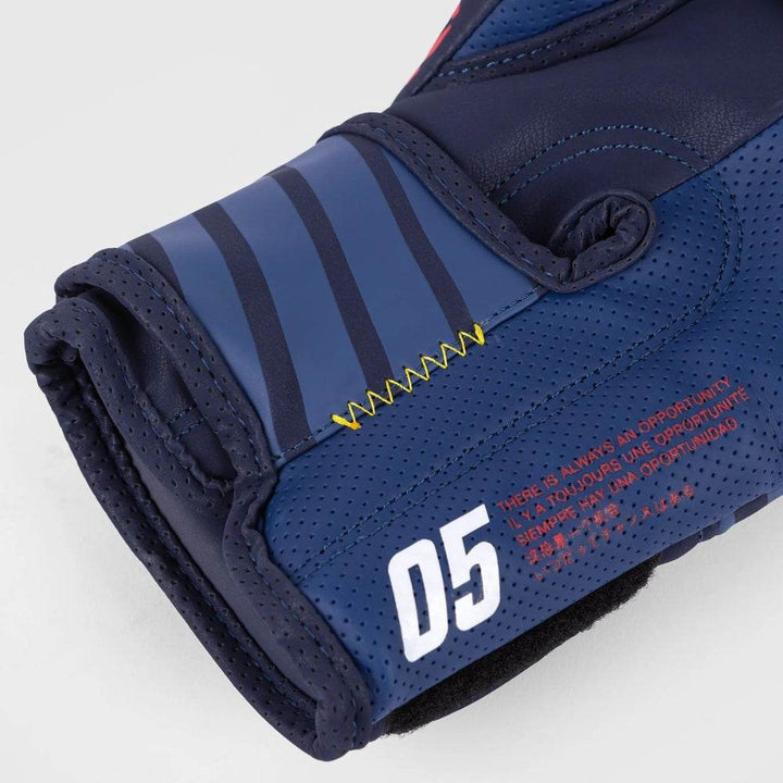 Close-up of glove’s wrist section highlighting yellow zigzag stitching and printed motivational quote in multiple languages, alongside number “05”.