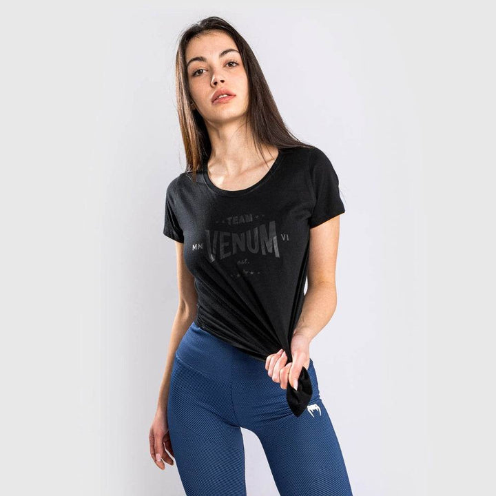 oman standing straight, wearing black Venum Team t-shirt and blue textured leggings.