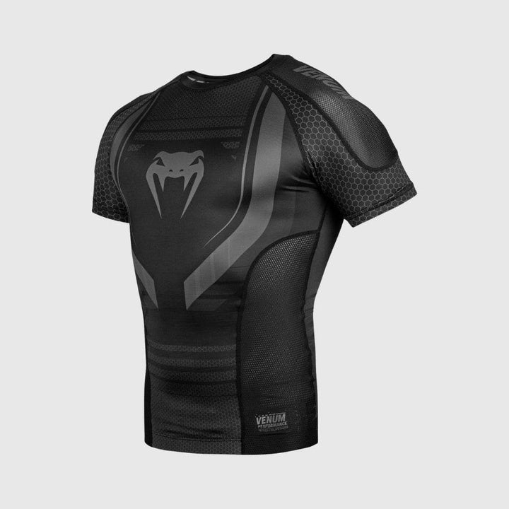 Three-quarter front view of the black Venum compression rash guard, showing muscular fit, mesh ventilation panels under the arms, and the tonal snakehead graphic on the chest.