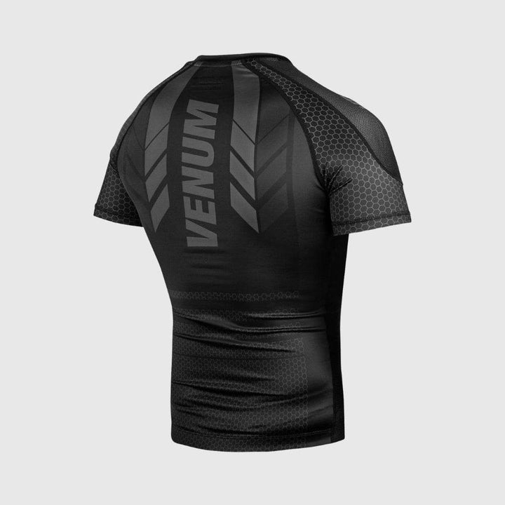Rear angled view of the black Venum rash guard, highlighting green VENUM branding and arrow detailing vertically aligned down the back.