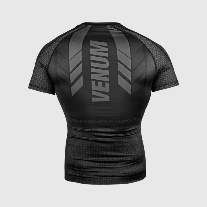 Direct back view of the black Venum rash guard, showcasing symmetrical design with green arrowhead graphics and bold VENUM lettering across the upper back.