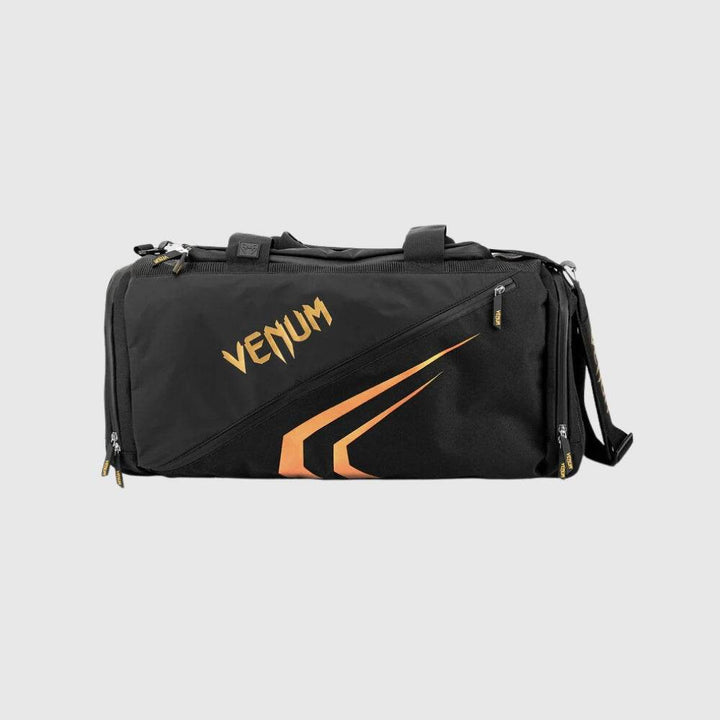 Side view of the Venum Trainer Lite EVO Sport Bag in black with bold gold VENUM logo and dynamic graphic design, featuring multiple zippered compartments and a detachable shoulder strap.