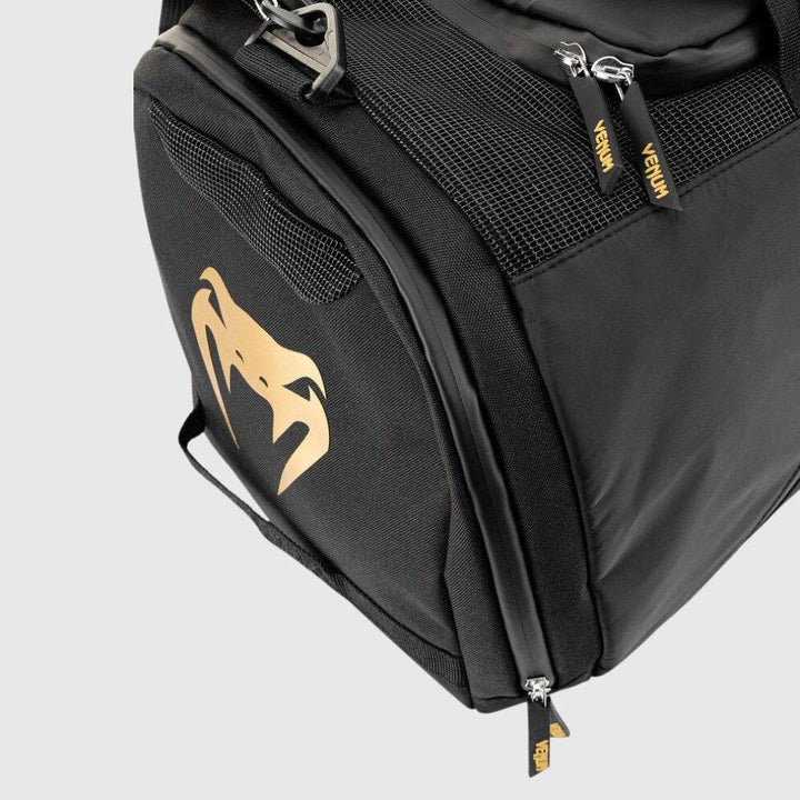 Close-up of the Venum Trainer Lite EVO Sport Bag's side compartment featuring the iconic Venum snakehead logo in metallic gold, mesh ventilation panel, and branded zipper pulls.
