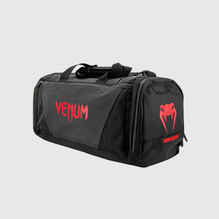Rear angled view of the Venum Trainer Lite EVO Sport Bag in black with red accents, showcasing bold VENUM text logo, snake emblem, and spacious side panel construction.
