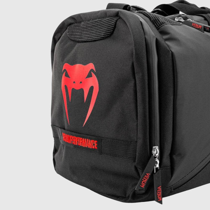 Close-up of the side pocket on the Venum Trainer Lite EVO Sport Bag in black with a red Venum snake logo and “HIGH PERFORMANCE” label stitched across the webbing.