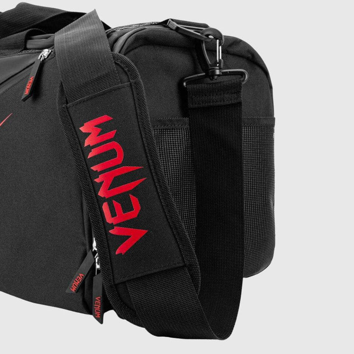 Close-up of the padded shoulder strap on the Venum Trainer Lite EVO Sport Bag, featuring bold red VENUM text and heavy-duty swivel clip attachment.