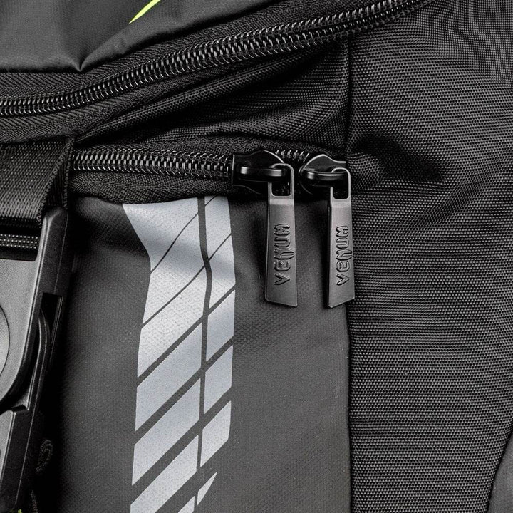 Close-up of the Venum backpack’s dual zipper pulls engraved with the VENUM logo, set against durable black fabric and reflective graphic detailing.