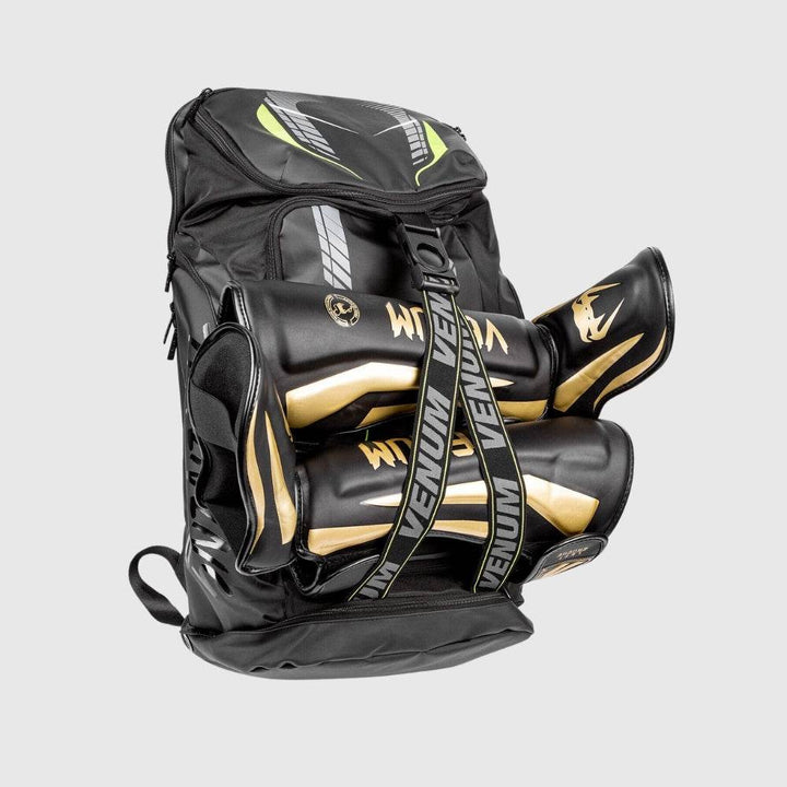 Venum backpack loaded with black and gold shin guards and boxing gloves, secured with front VENUM-branded elastic straps.