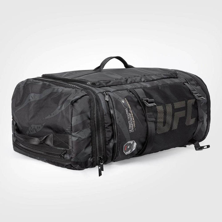 Angled rear view of the UFC Fight Week Performance Kit bag by Venum, highlighting the large mesh UFC logo panel, dual zippered compartments, and reinforced side grab handle.