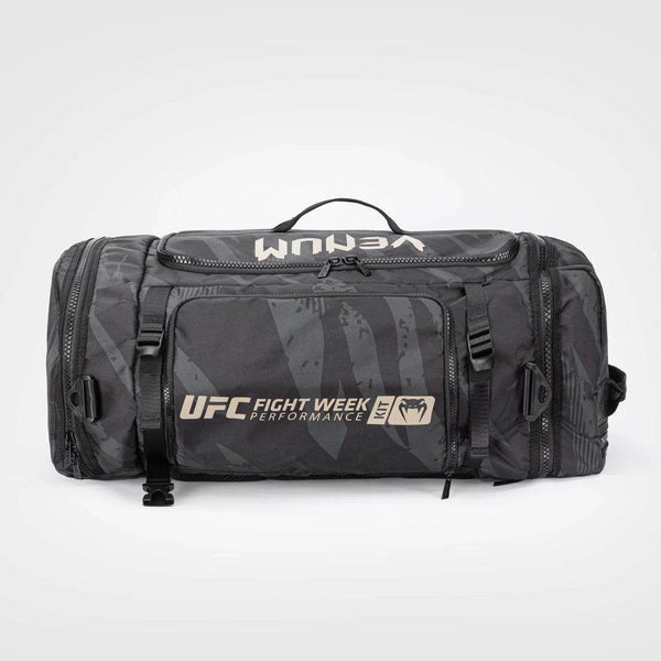 Front view of the UFC Fight Week Performance Kit sport bag by Venum in black with tan accents, featuring bold "UFC Fight Week" branding, multiple zippered compartments, and compression straps.