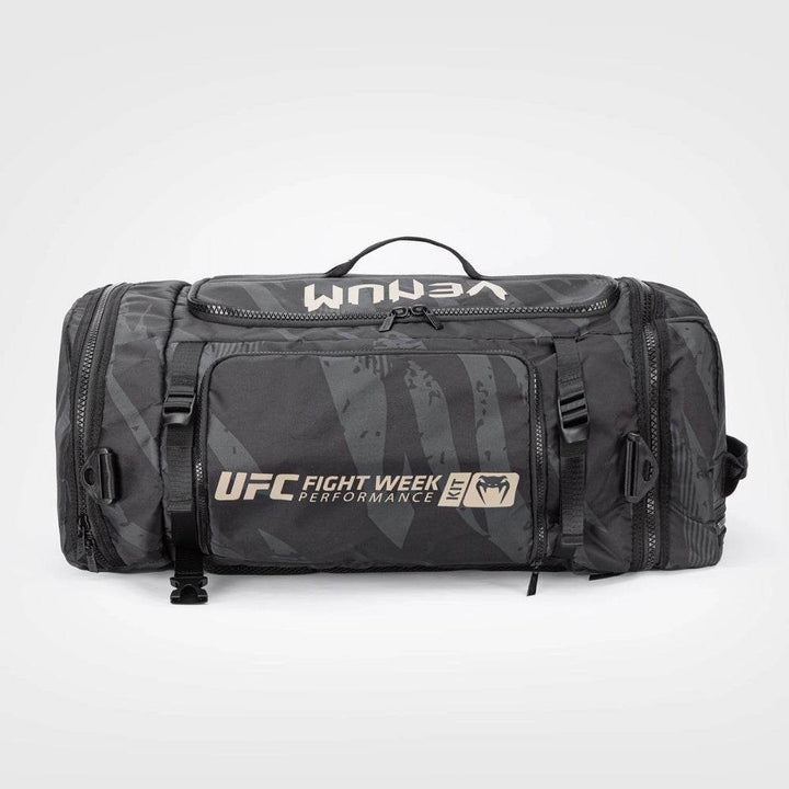 Front view of the UFC Fight Week Performance Kit sport bag by Venum in black with tan accents, featuring bold "UFC Fight Week" branding, multiple zippered compartments, and compression straps.