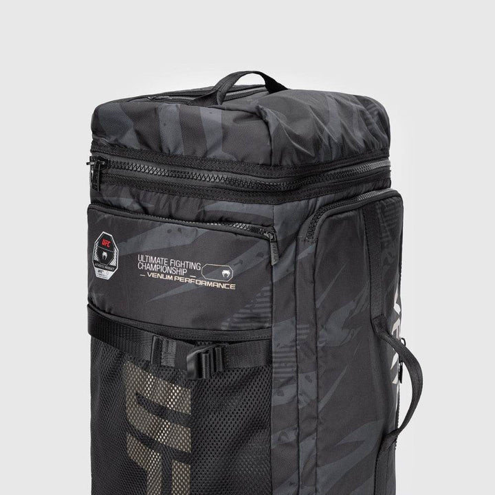 Close-up of the upper side panel of the UFC Fight Week Performance Kit bag by Venum, featuring dual zippers, grab handle, mesh UFC logo pocket, and "Ultimate Fighting Championship – Venum Performance" patch.