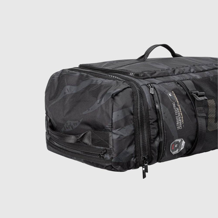 Close-up of the side panel of the UFC Fight Week Performance Kit bag, showing durable black fabric with subtle camo pattern, reinforced grab handle, and multiple zippered compartments.