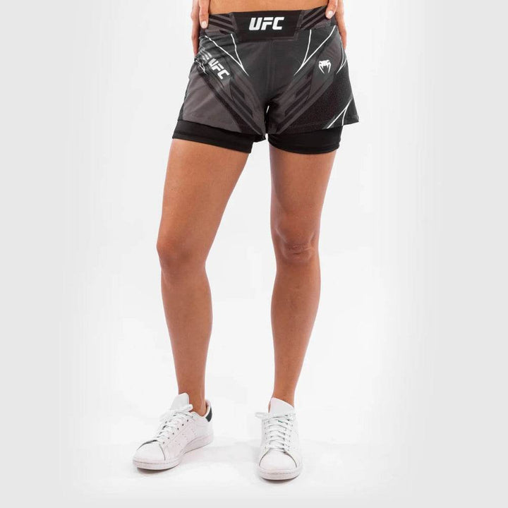 A close-up view of the front of the black UFC Venum women's fightshorts, highlighting the dual-layer design with integrated compression shorts and white UFC branding.