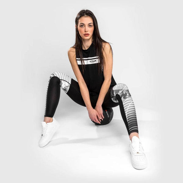 Female athlete wearing black and white Venum leggings with samurai-themed artwork, squatting on a medicine ball.